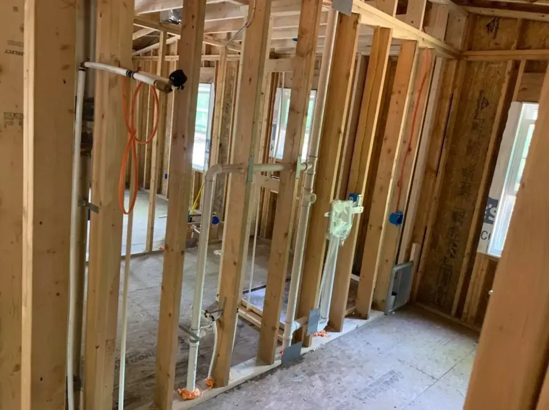 Unfinished house interior with exposed wooden studs and framing, showing a hallway and open rooms.