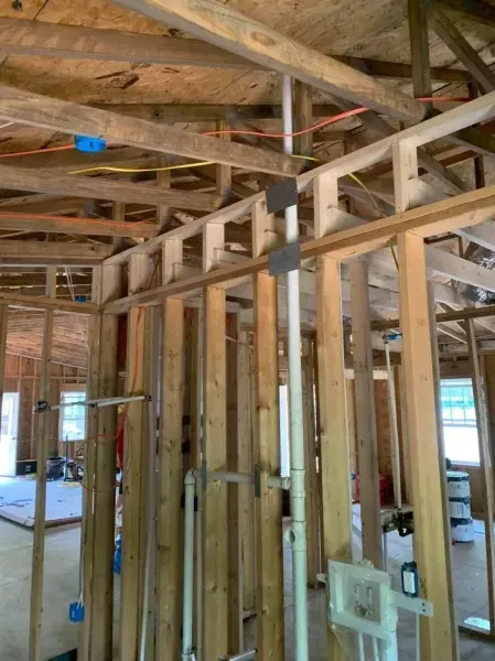 Interior framing of a house under construction with exposed wooden studs, ceiling joists, and wiring