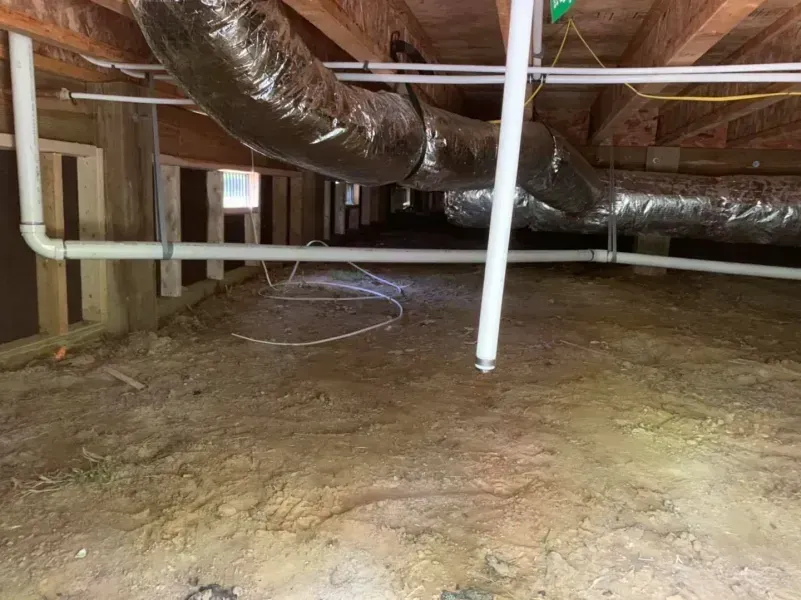 Crawlspace with exposed ductwork, pipes, and dirt floor under a house