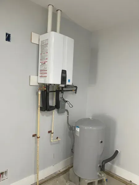 Wall-mounted water heater and gray pressure tank in a utility room with exposed pipes