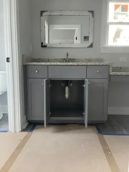 Bathroom vanity with open cabinet doors, gray cabinets, granite countertop, and wall mirror under construction