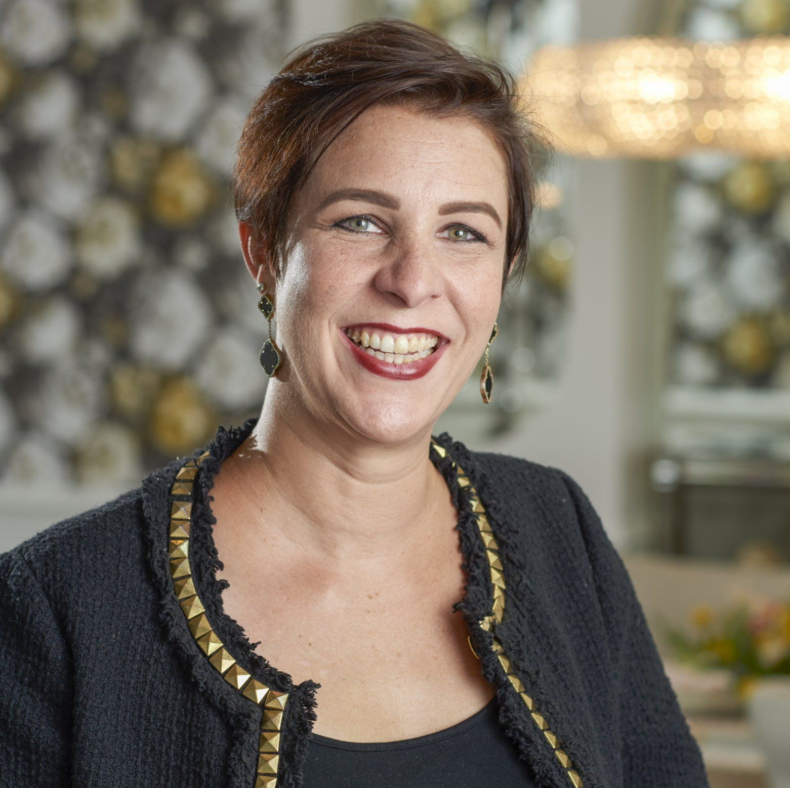 A woman wearing a black jacket and earrings smiles for the camera