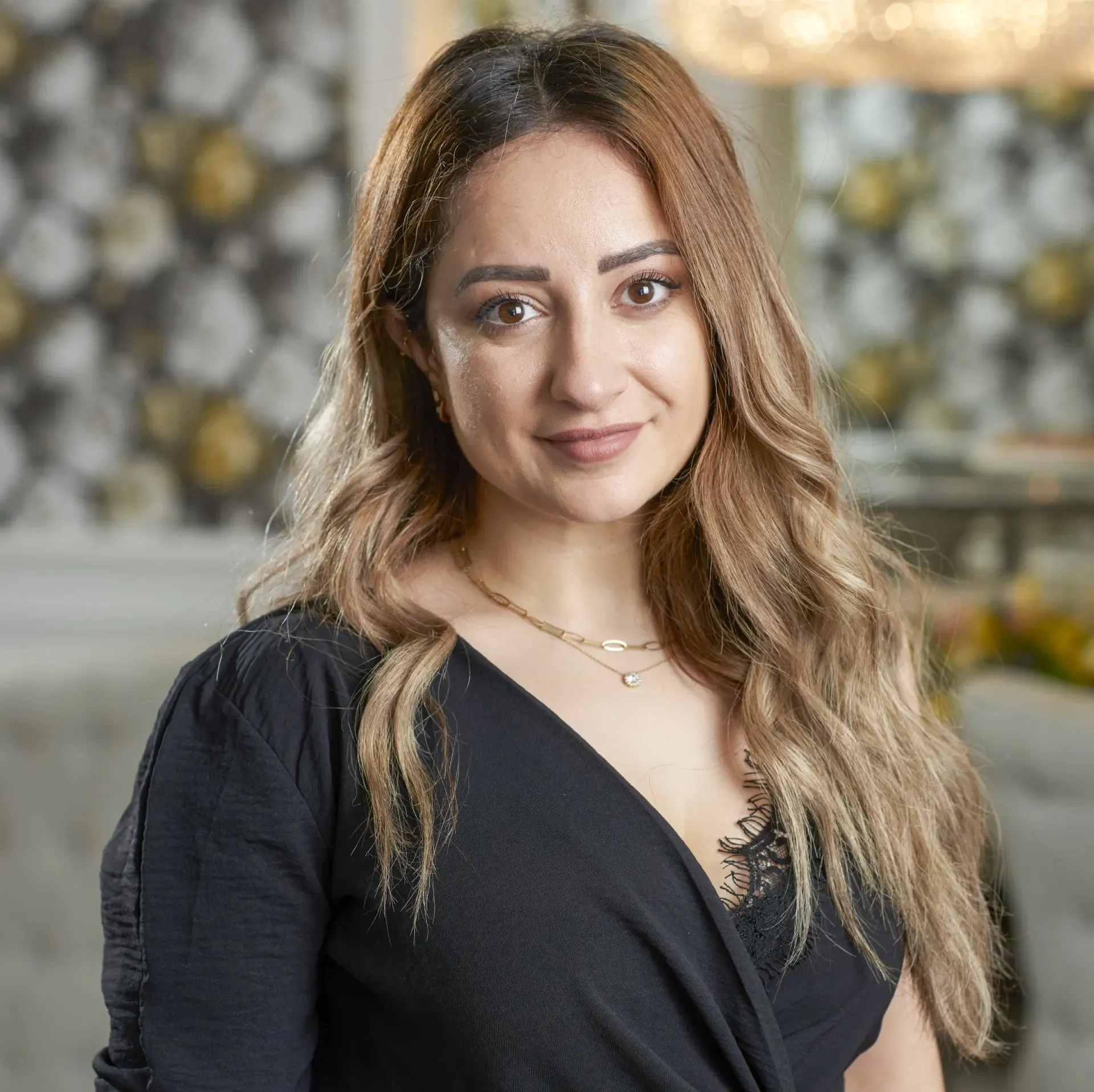 A woman with long hair is wearing a black top and a gold necklace.