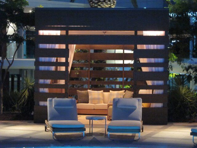 A cabana with a couch and chairs in front of a swimming pool