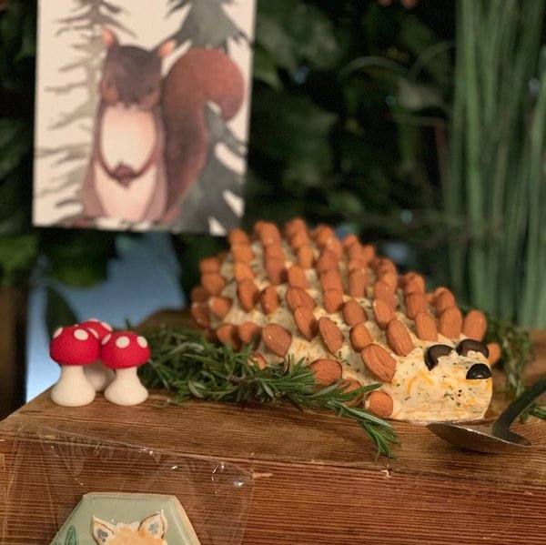 A hedgehog made out of nuts is sitting on a wooden table next to a picture of a squirrel.