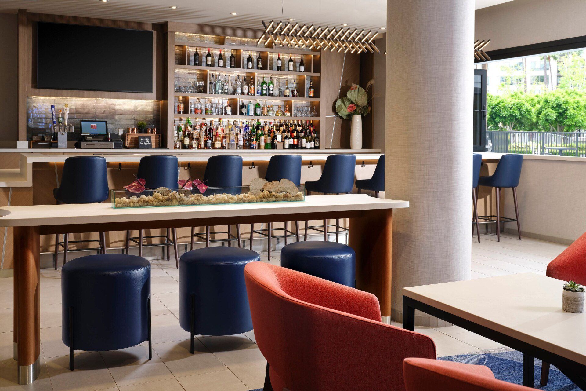A hotel lobby with a bar , chairs , tables and stools.