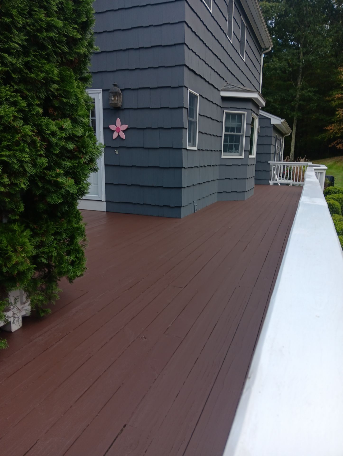 A side view of a house with dark gray siding, a brown deck, and a white railing, featuring a small pink flower decoration.