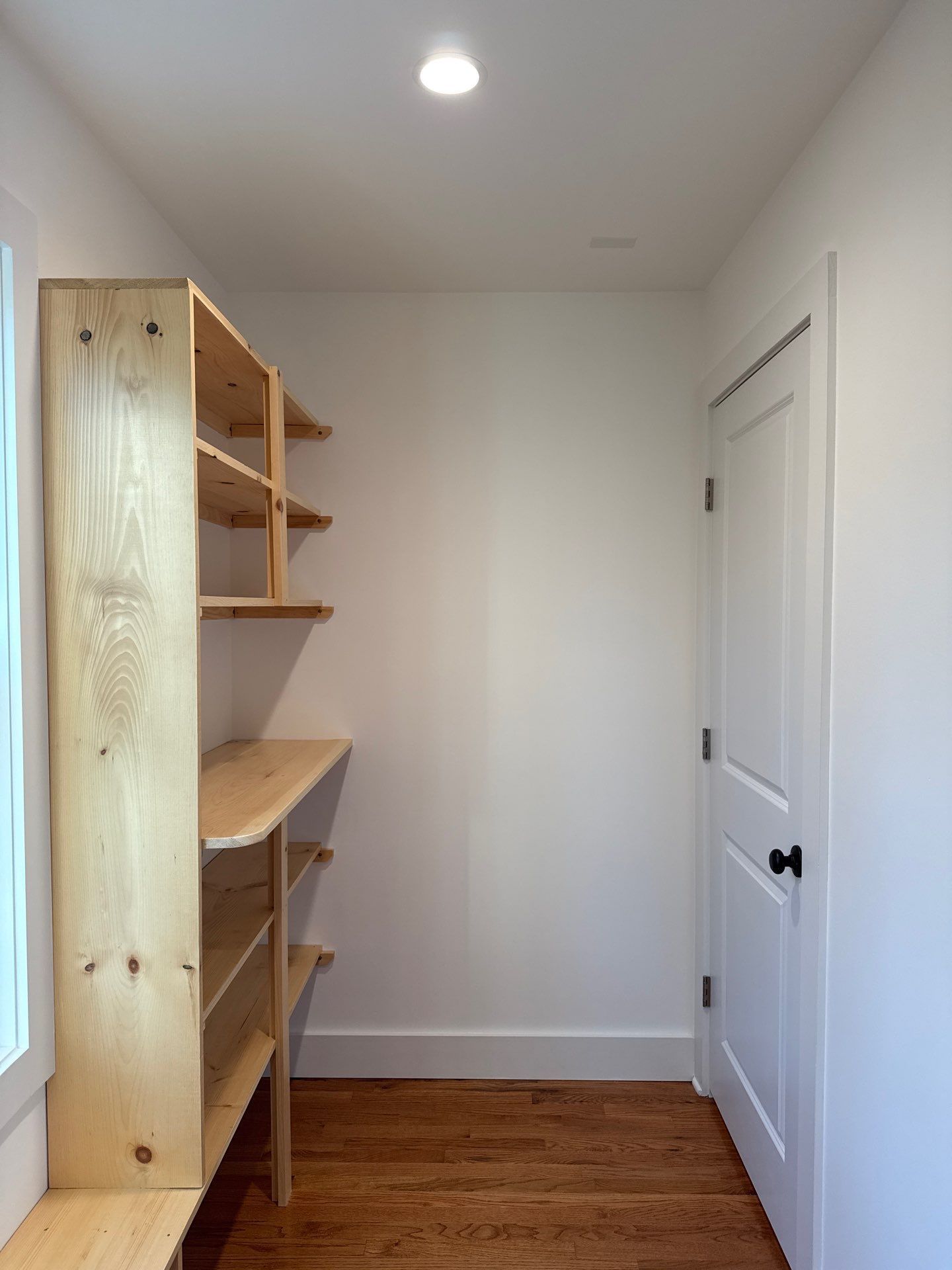 A small closet featuring light wood shelving on the left wall, white walls, and a white door on the right.