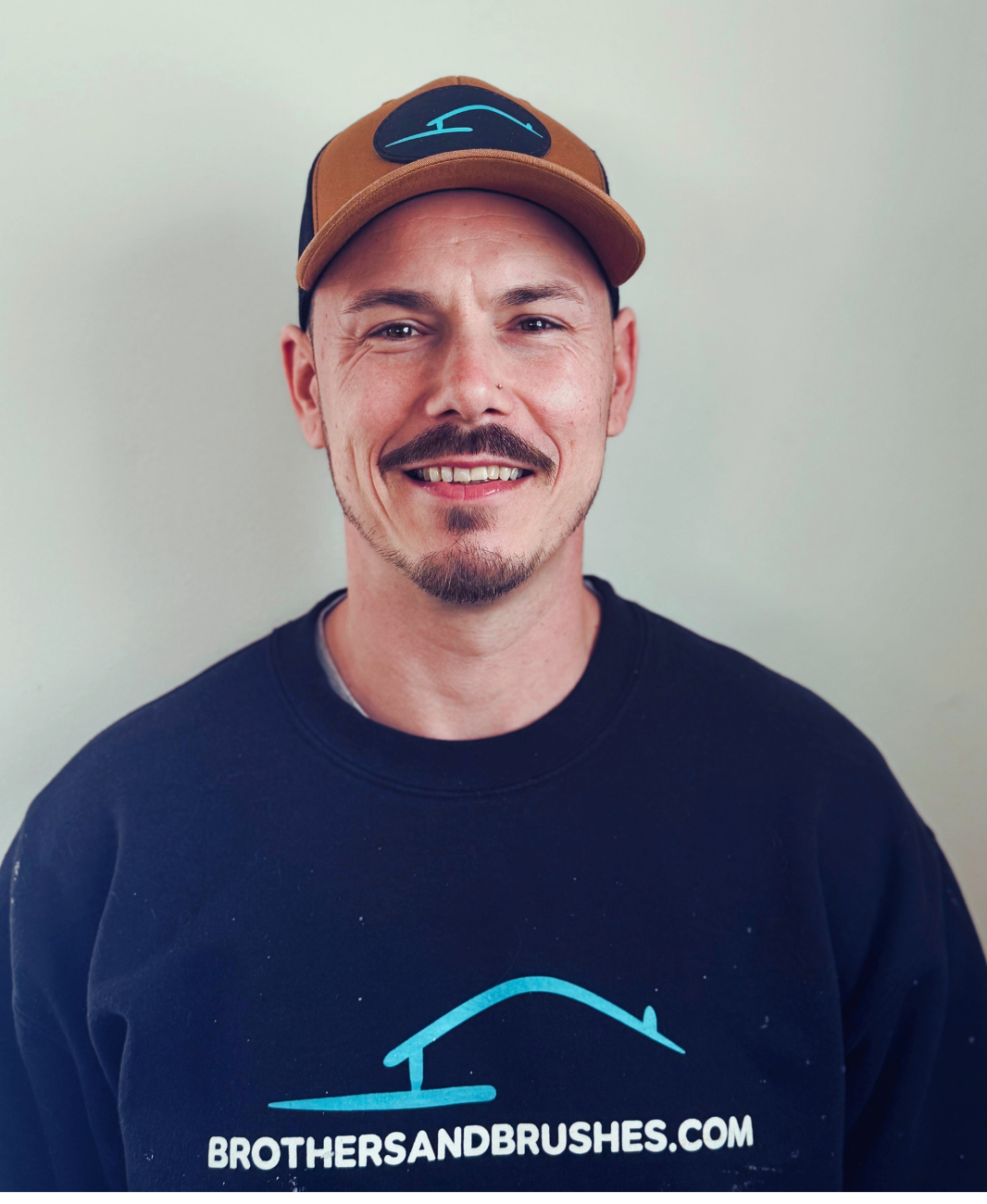 A smiling person wearing a brown cap and a black long-sleeved shirt with 