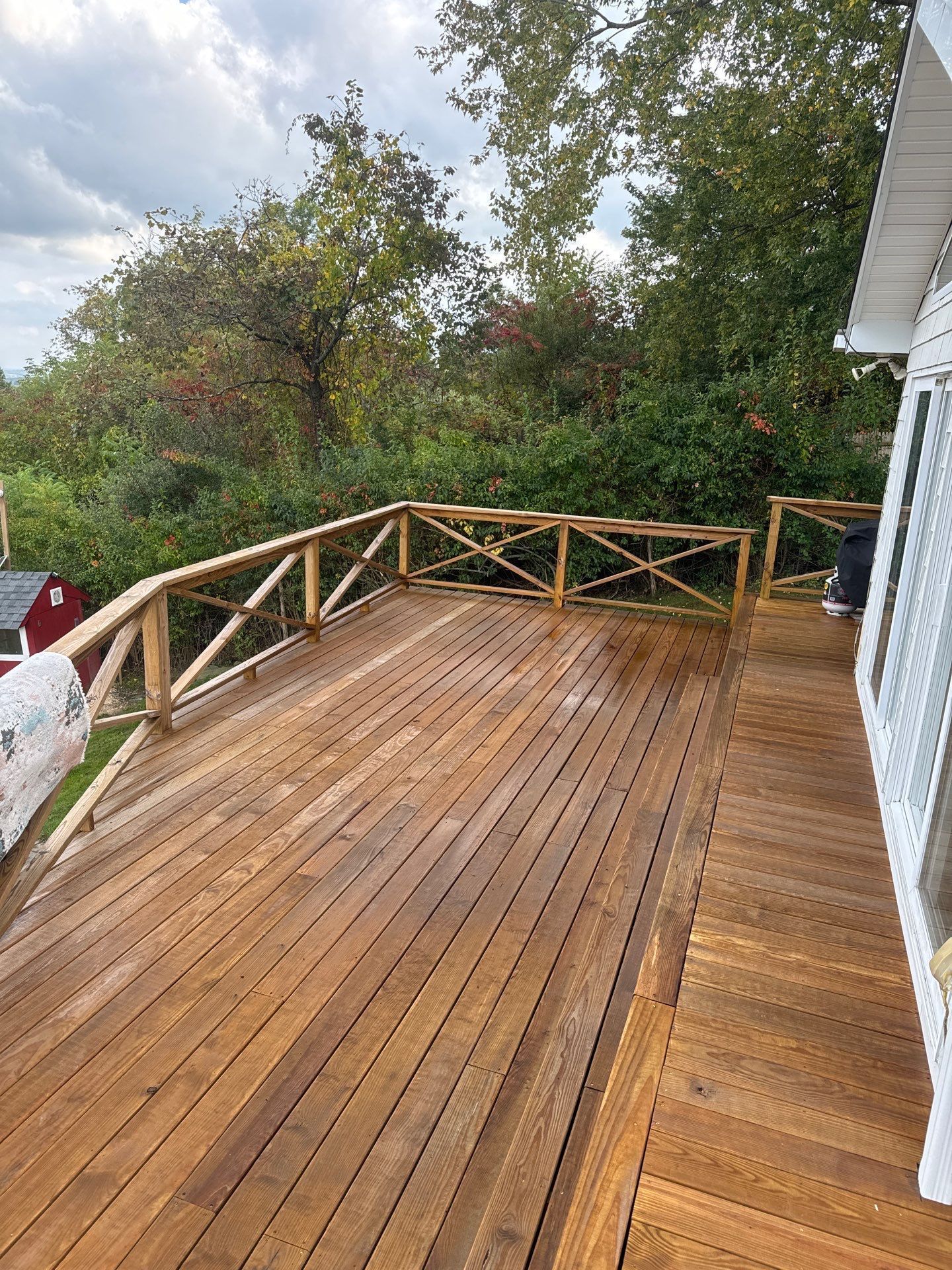 A freshly stained wooden deck with lattice railing extends from a white house toward a lush green backyard.