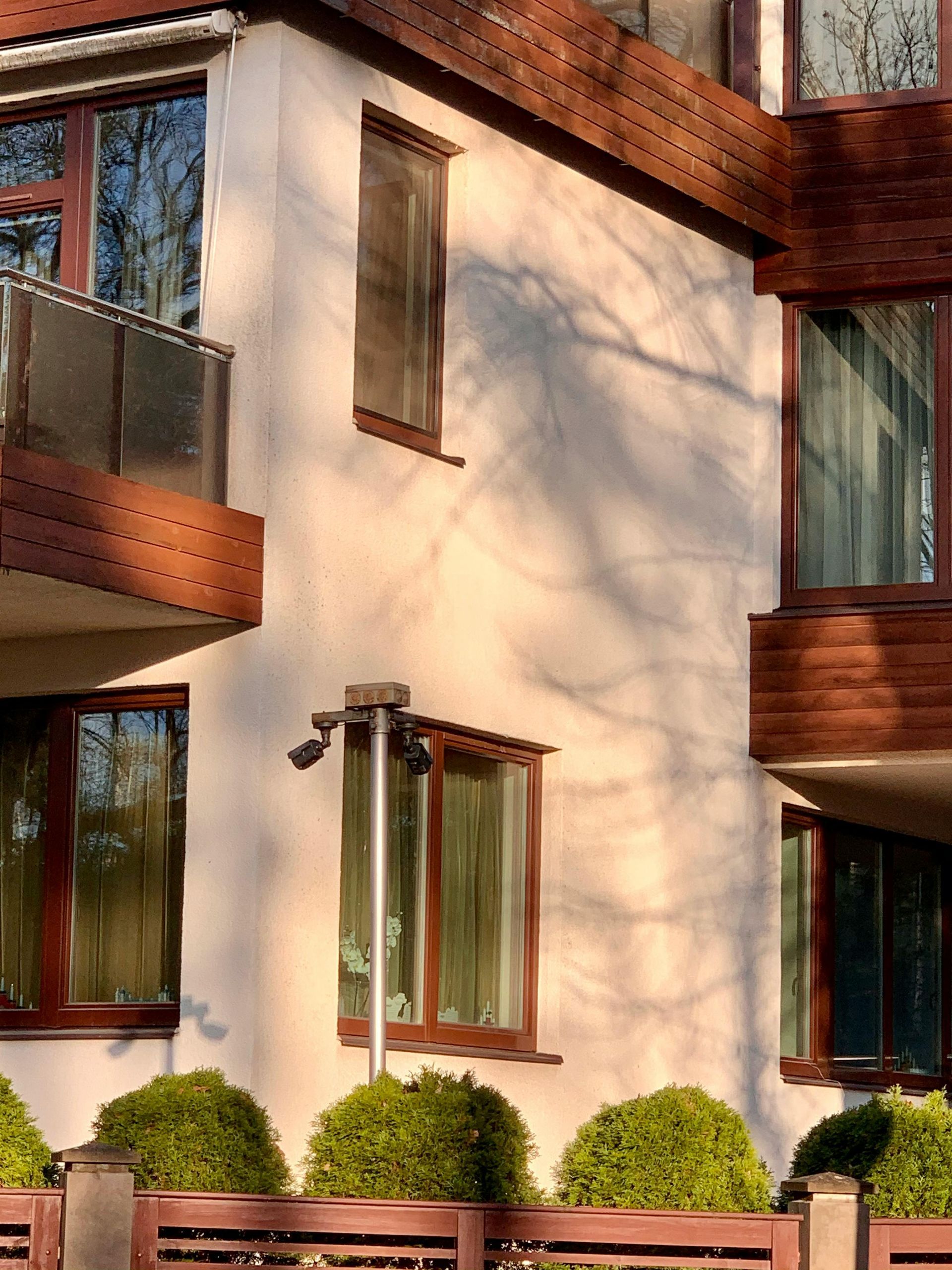 Cream-colored building exterior with brown wood trim, balconies, windows, and green landscaping in front.