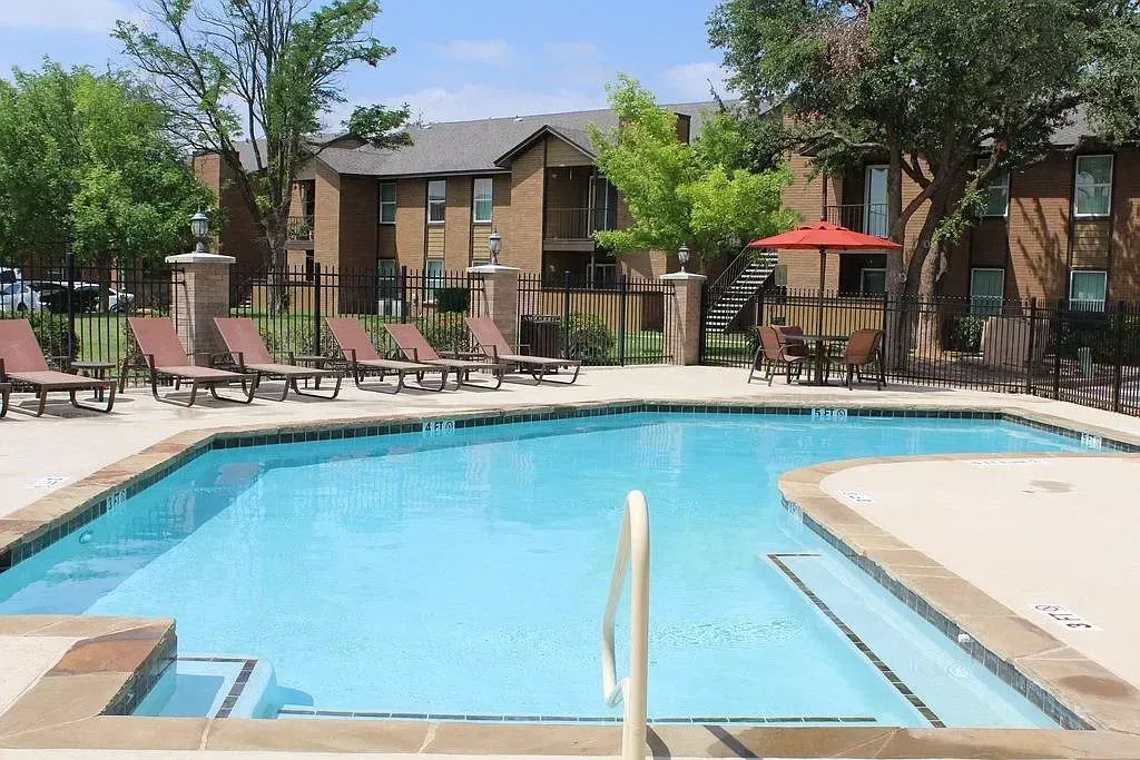 Outdoor swimming pool with lounge chairs and a table with umbrellas.