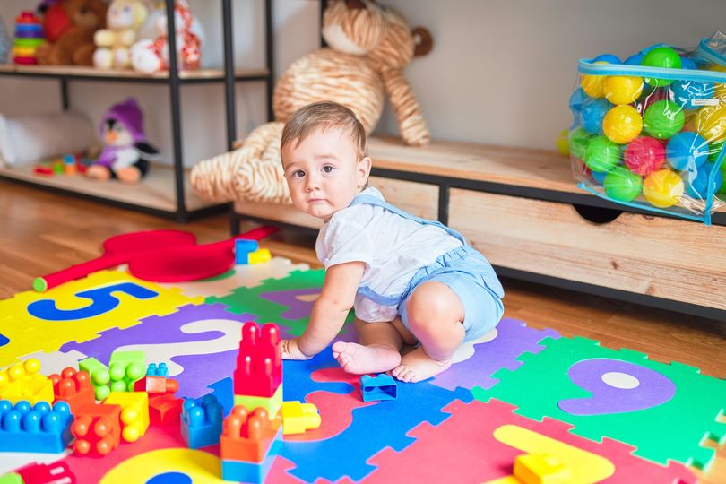 A baby is sitting on a puzzle mat playing with toys.