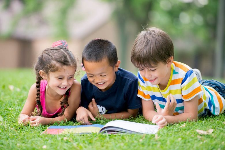 Smiling children reading a book together on grass