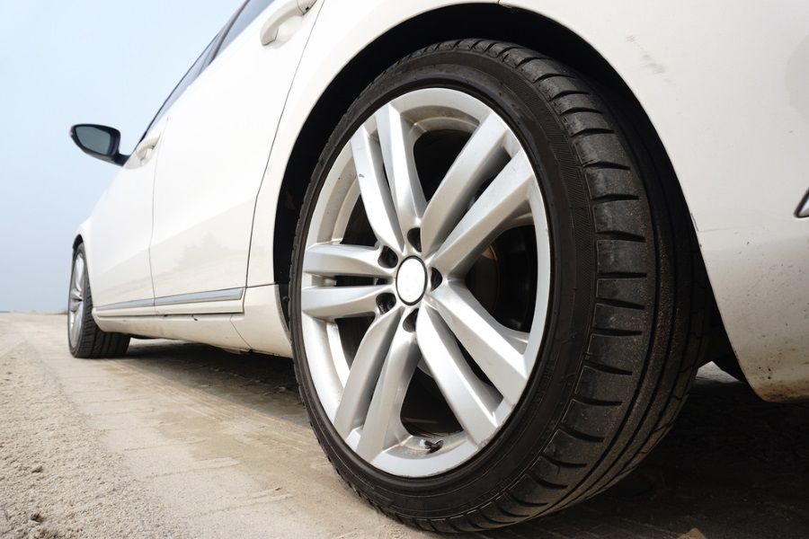 A Close-up of a White Car's Front Wheel With a Silver Alloy Rim and Tire, on a Sandy Surface — City Tyre Service in Darwin City, NT