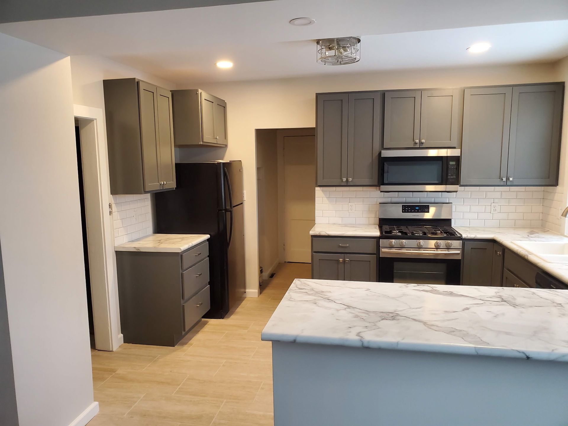Modern kitchen with gray cabinets, marble countertops, stainless appliances, and light wood flooring.