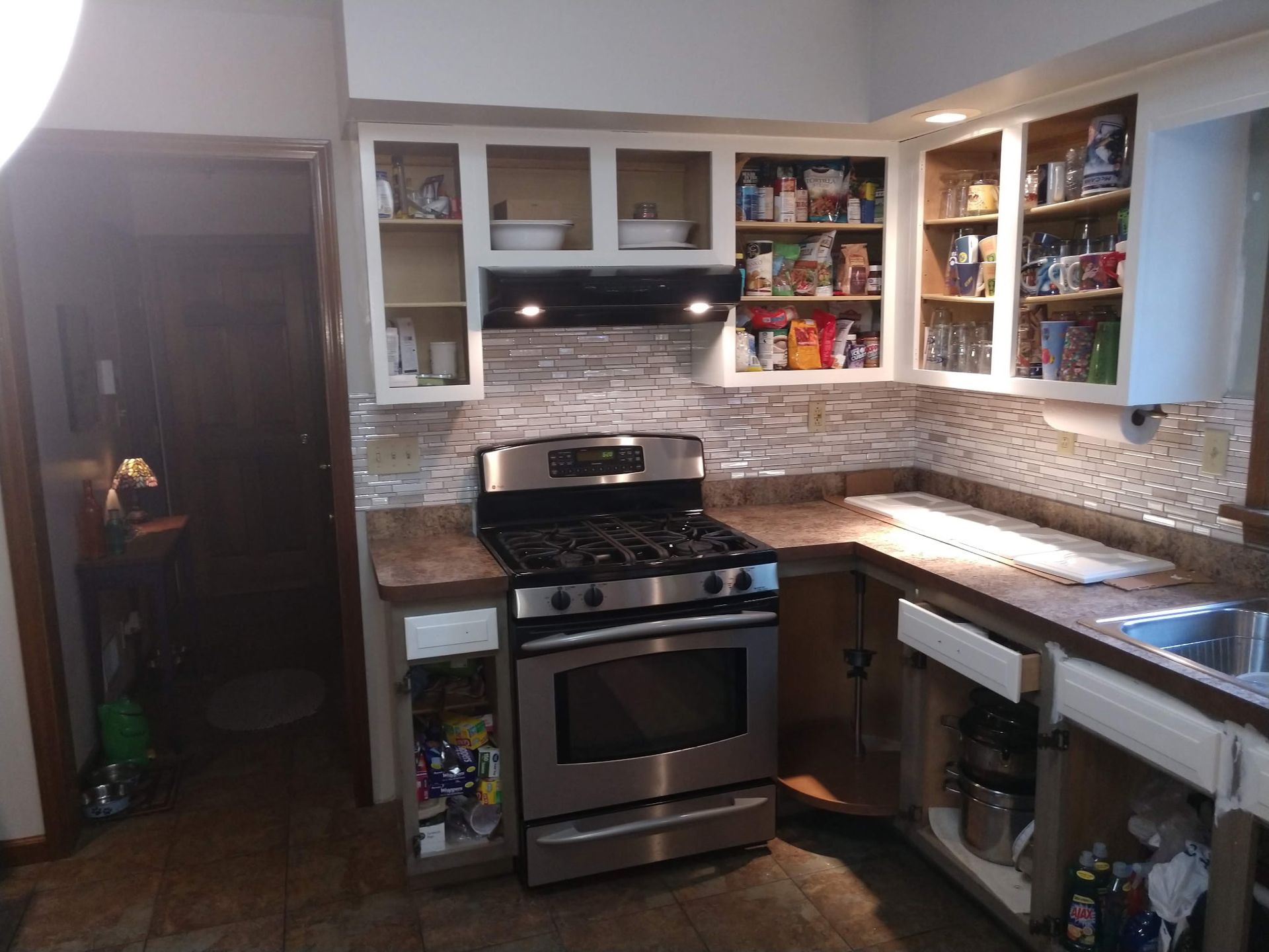 Compact modern kitchen with stainless stove, white cabinets, and mosaic tile backsplash
