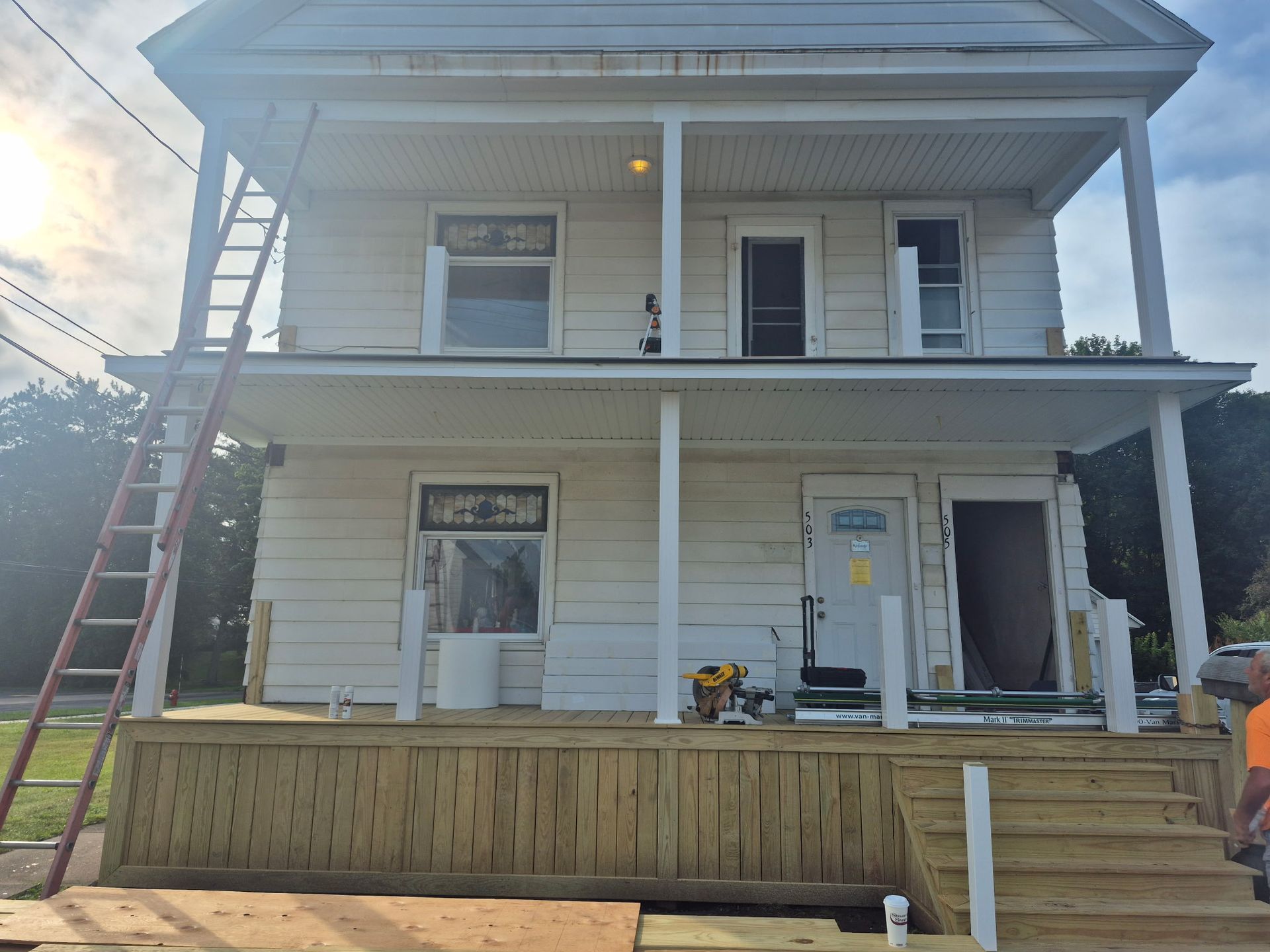 Two-story white house with front porch, stairs, and a red ladder leaning on the left side