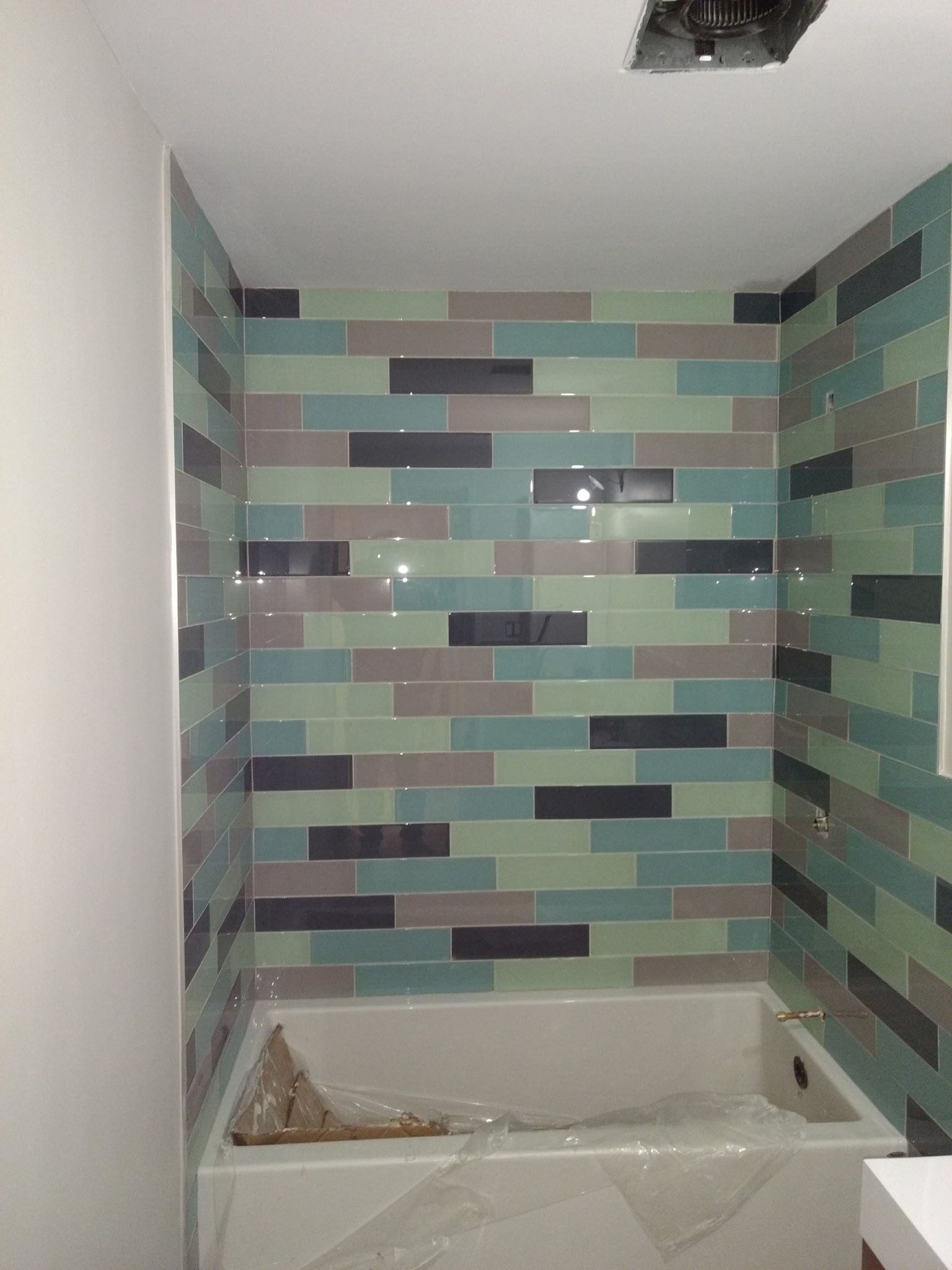 Partially tiled bathroom with a bathtub, multicolored horizontal wall tiles, and a ceiling light opening