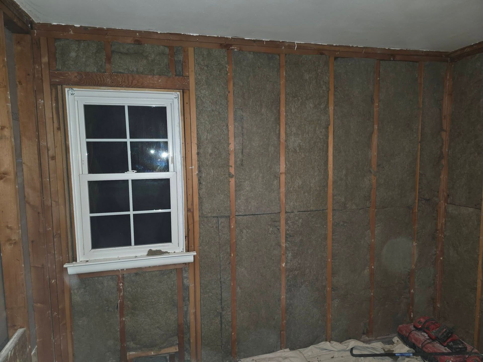Unfinished room with exposed wall framing, insulation, and a small window.