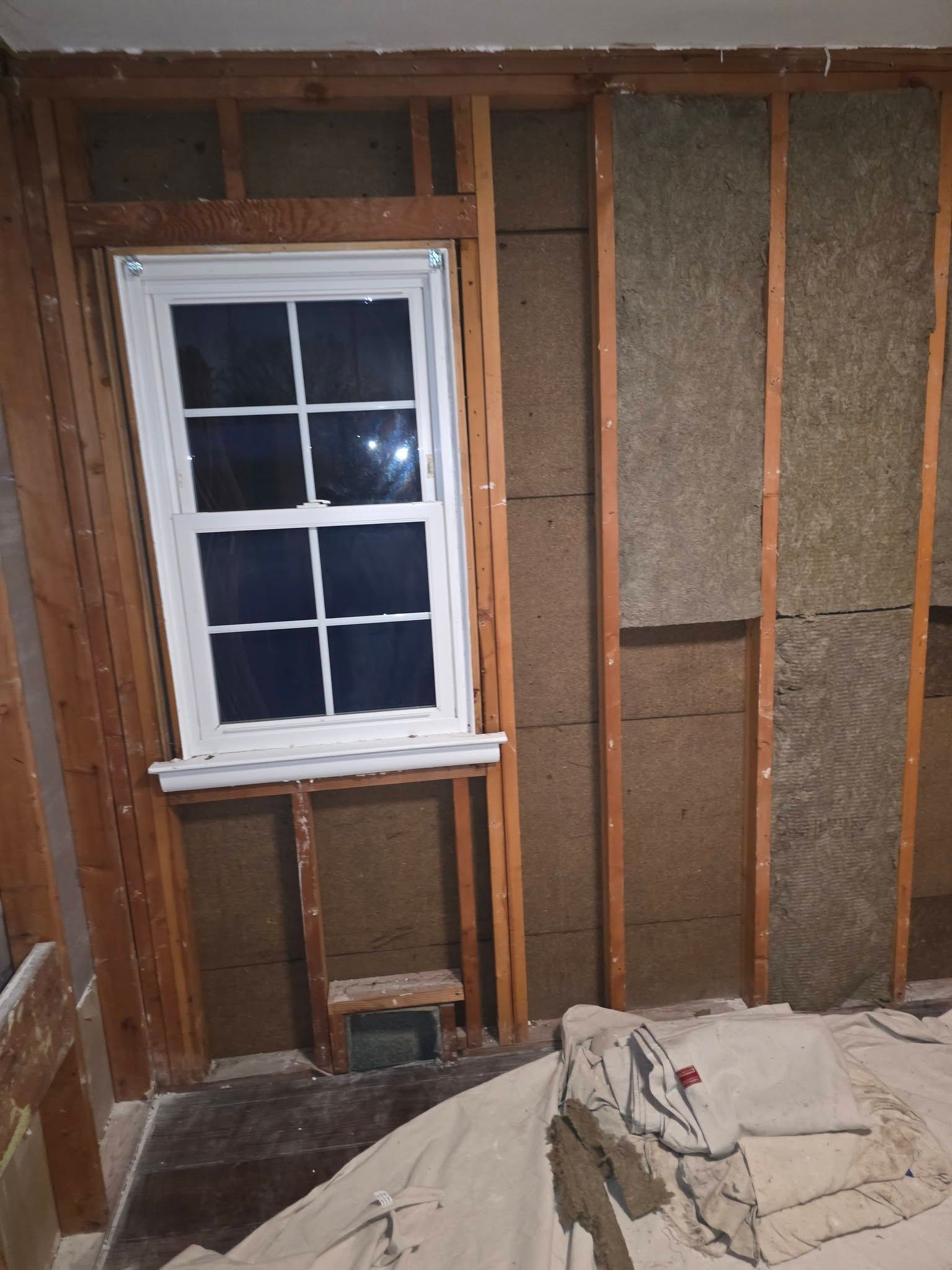 Unfinished room with exposed wall studs, insulation, and a white-framed window above a bare opening.
