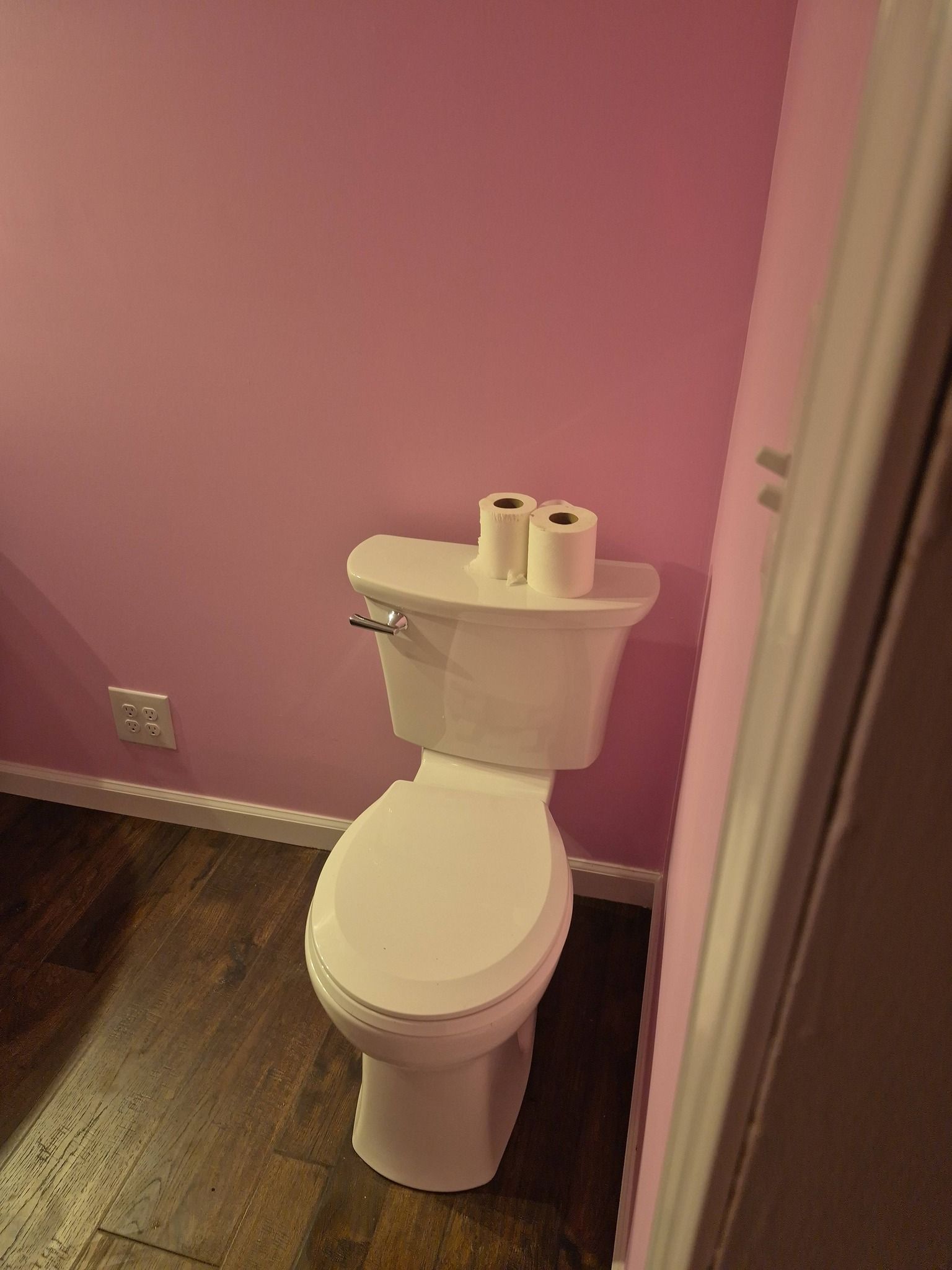 Pink bathroom with a white toilet against the wall and dark wood floor.