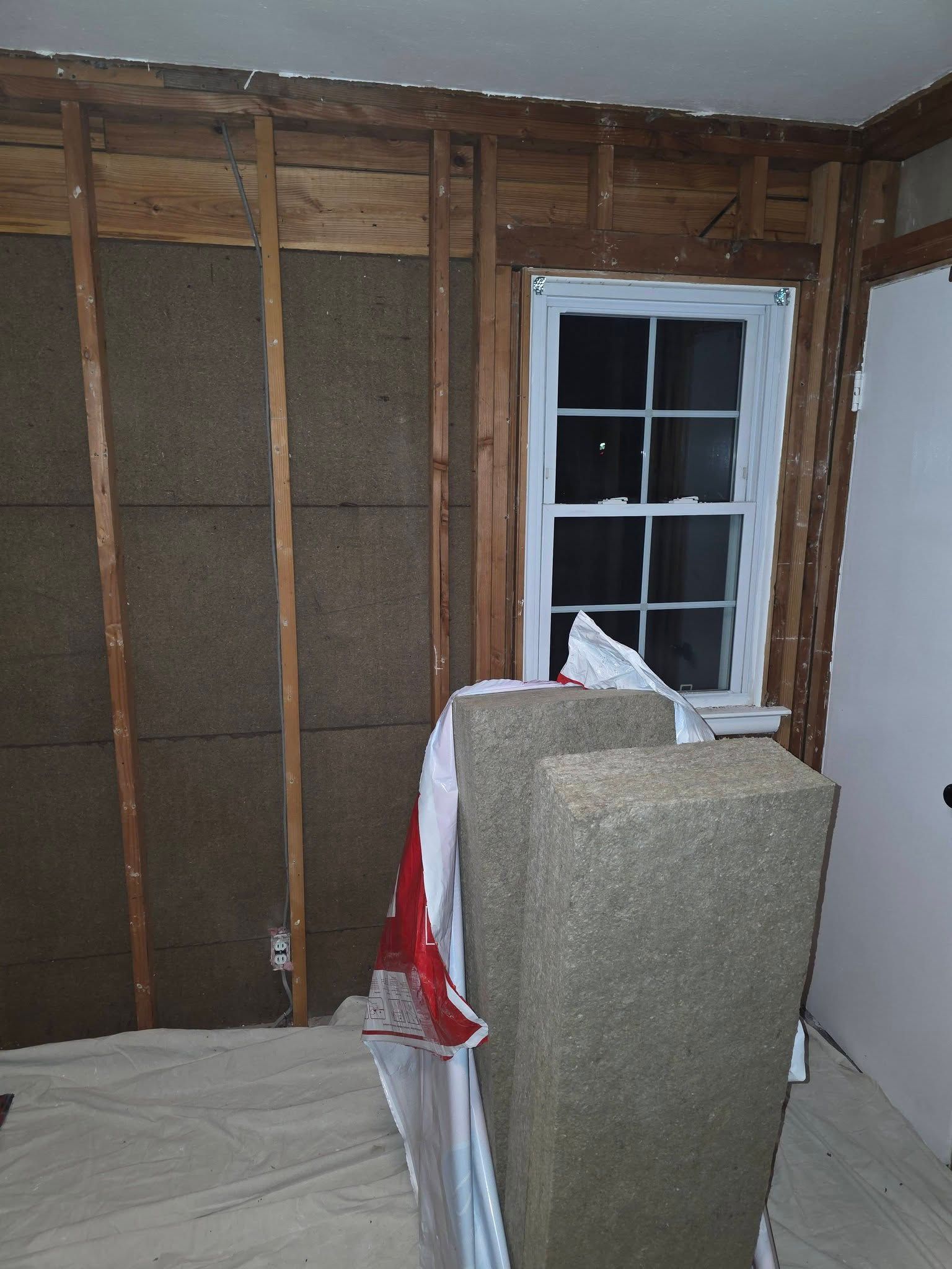 Unfinished room with exposed wall studs, a window, and a covered object in the foreground.