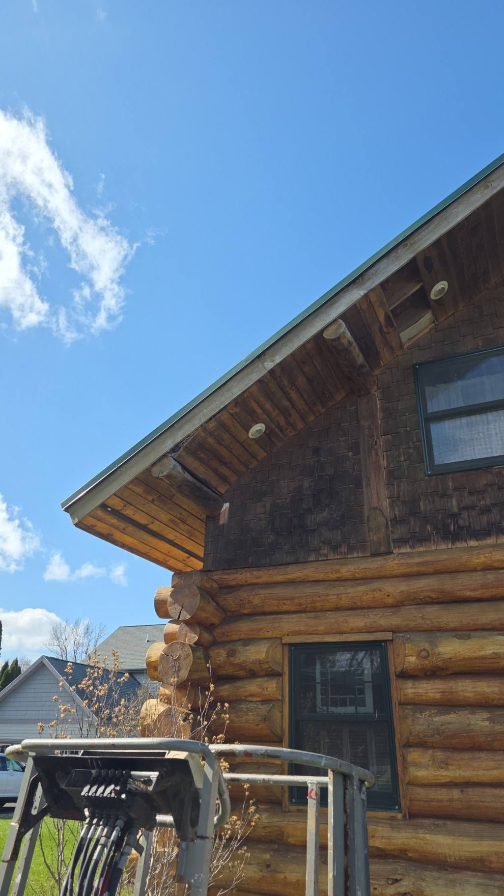 Wooden log cabin under a bright blue sky, with a porch and a vehicle in the foreground.