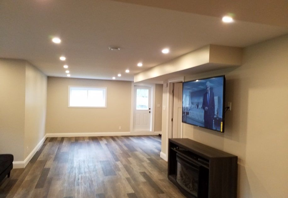 Empty basement family room with recessed lights, wood flooring, and a wall-mounted TV.