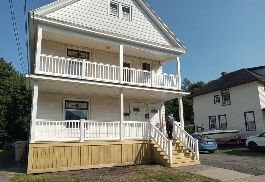 Two-story white house with porches and steps in a residential neighborhood