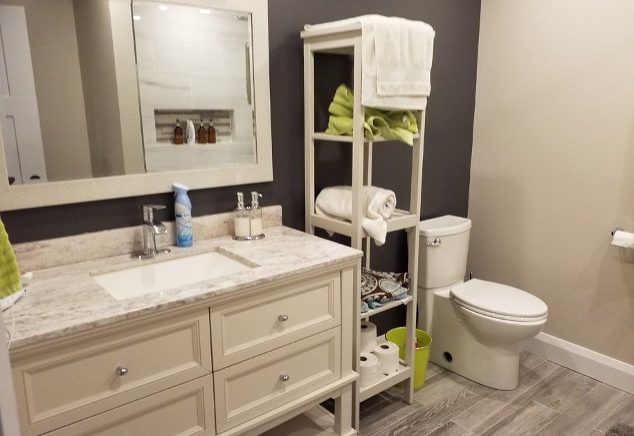 Modern bathroom with vanity, mirror, shelving, and toilet in beige and gray tones