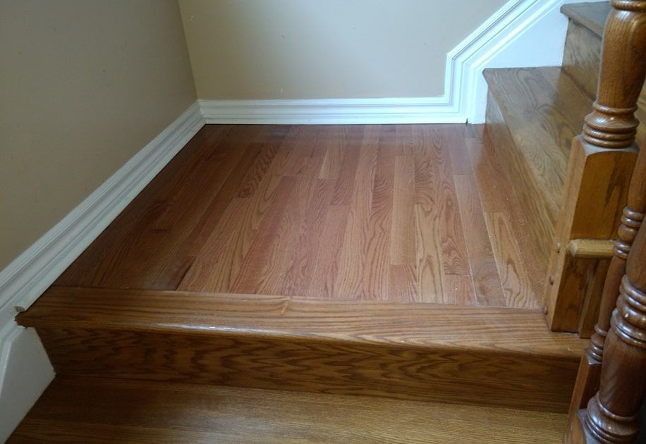 Wooden stair landing with white trim and beige walls beside a carpeted staircase