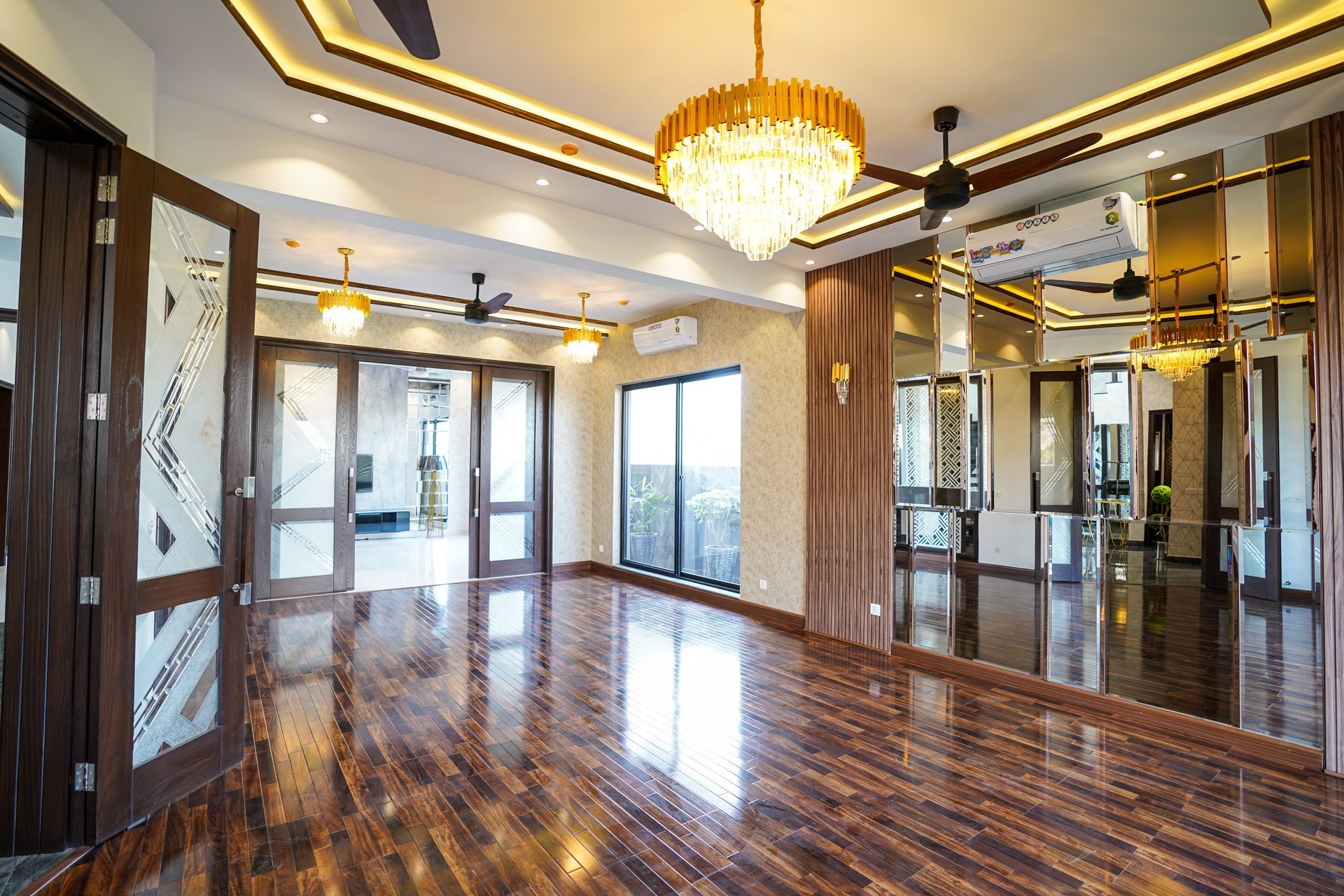 Empty luxury living room with polished wood floor, crystal chandelier, and mirrored walls