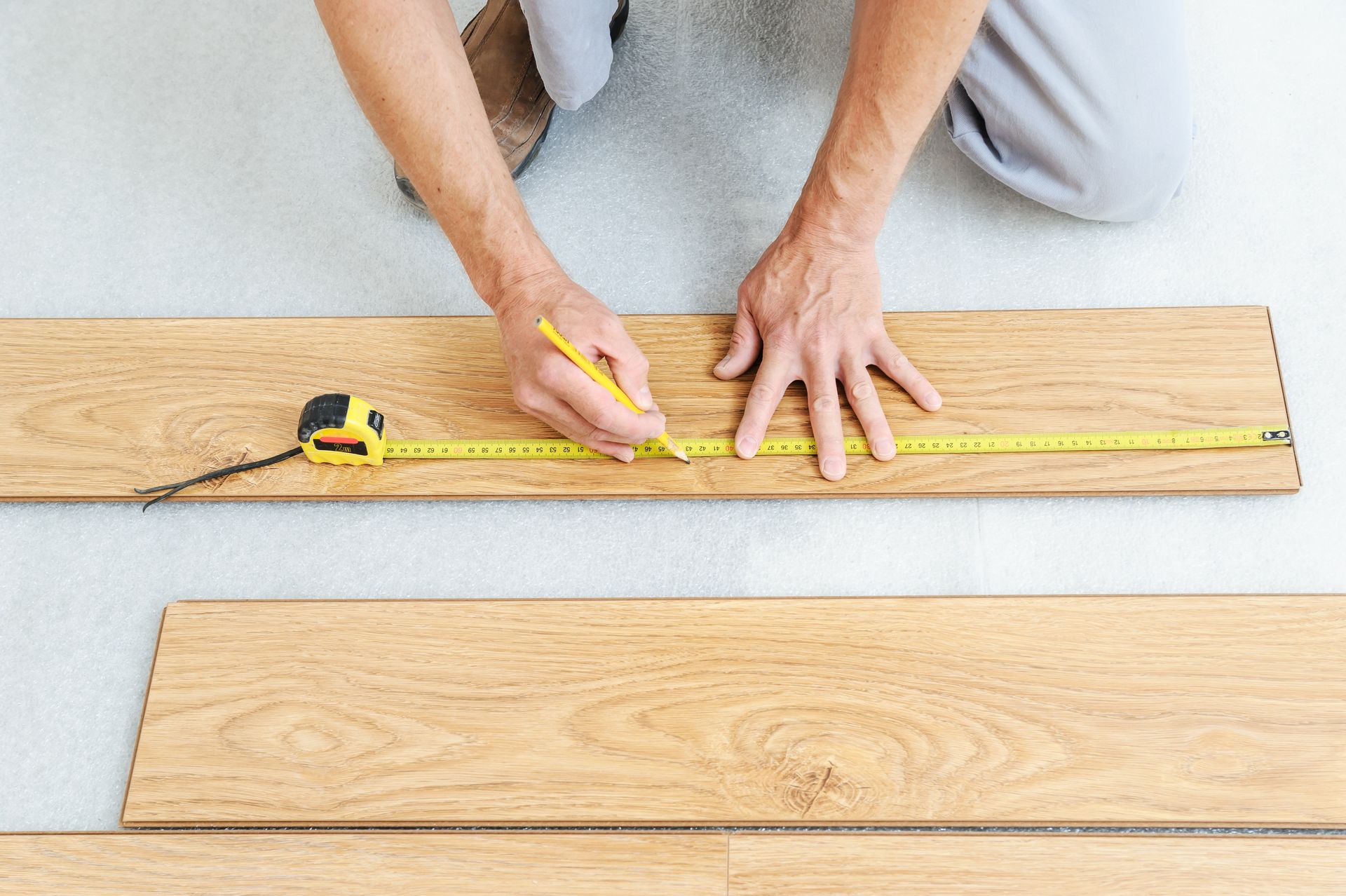 A man is measuring a piece of wood with a tape measure.