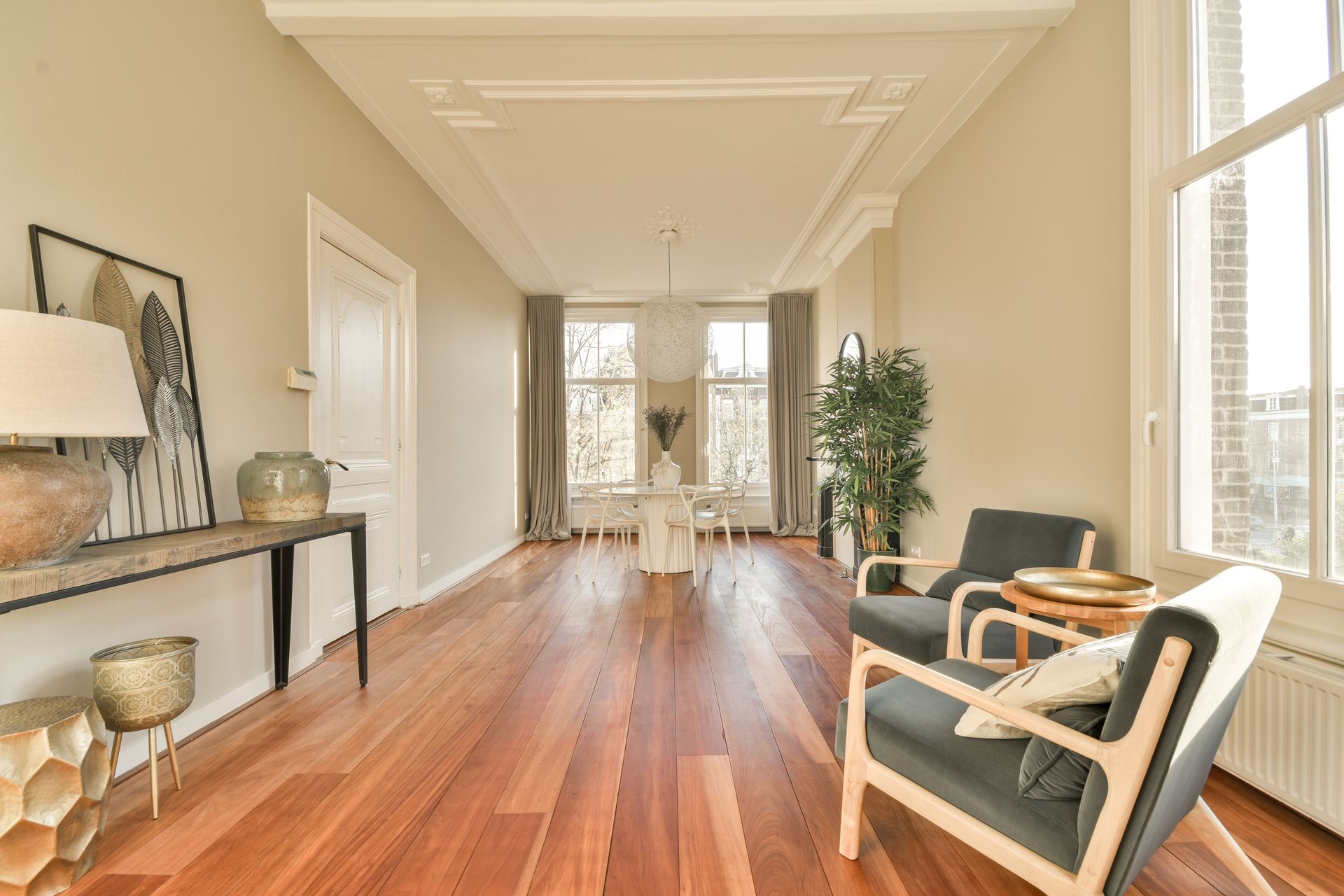 Bright hallway with wood floors, white walls, black sideboard, and armchairs by tall windows.
