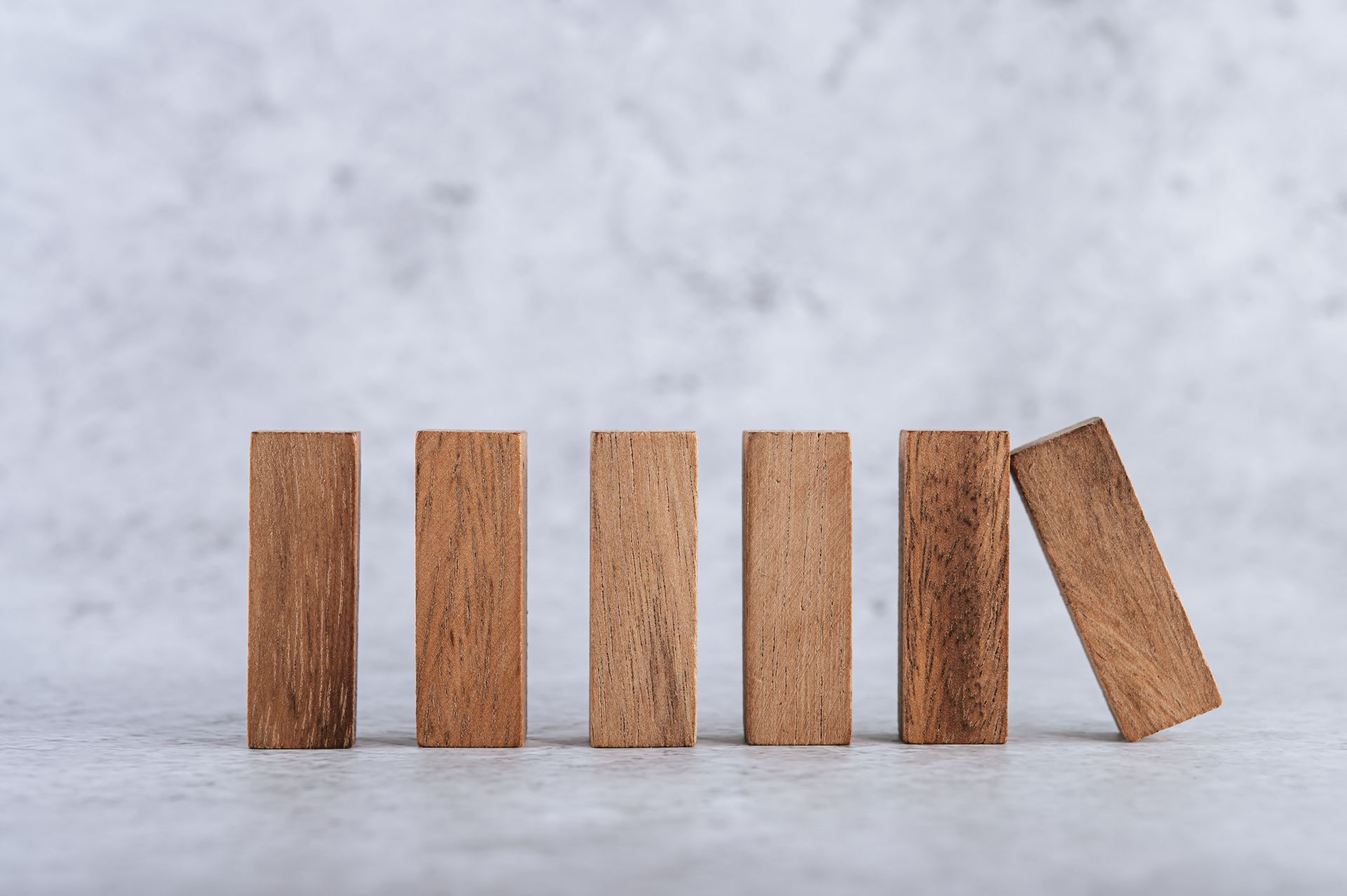 Six wooden blocks standing in a row, with one block leaning outward at the end.