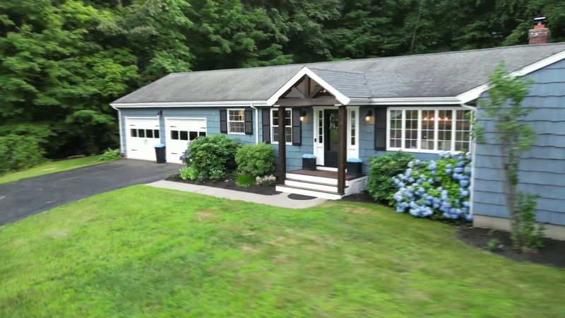 Front exterior of 12 Pond Road in Canton, with a blue-gray facade, lawn and flowering hydrangeas