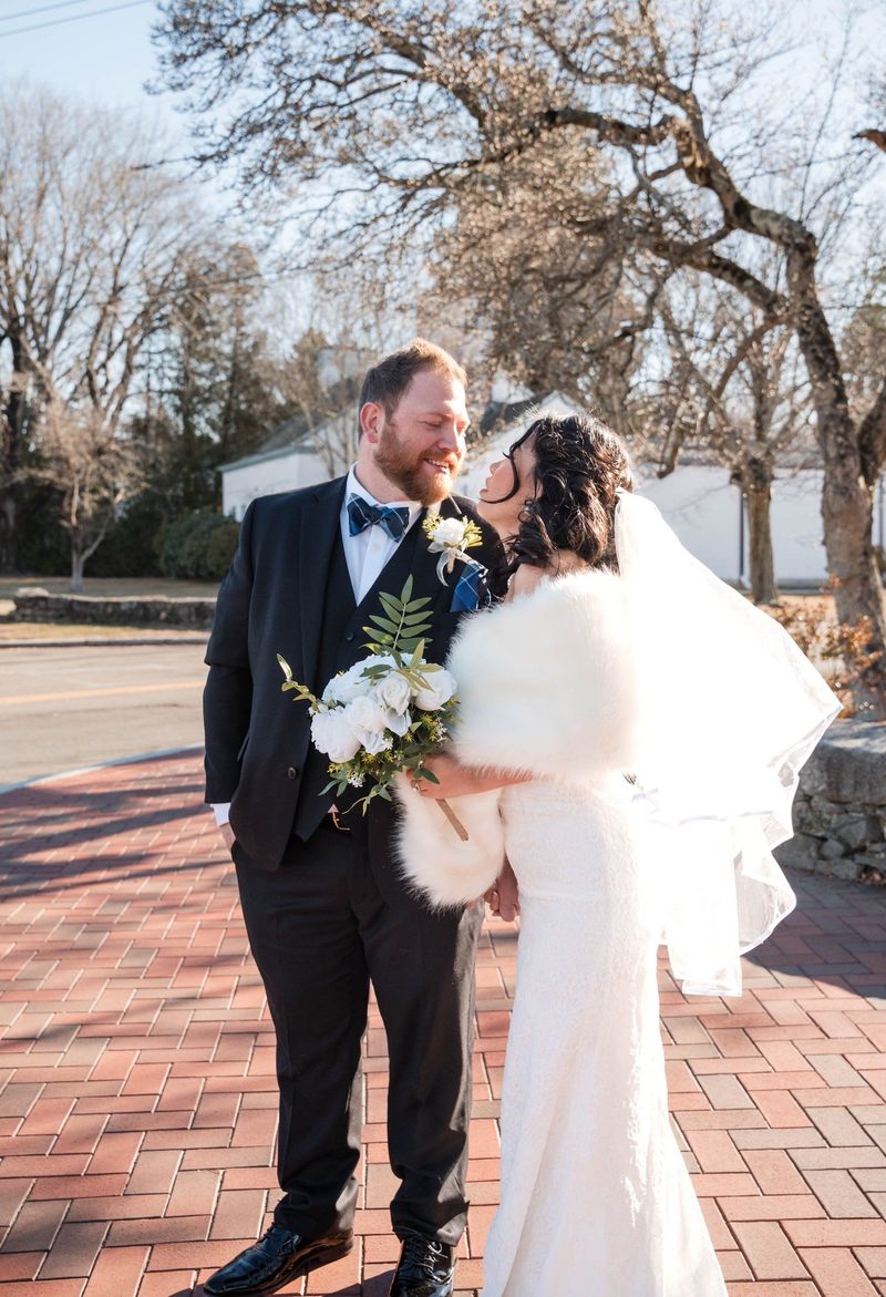 Amanda and Charles look toward each other on a brick sidewalk beneath bare tree branches