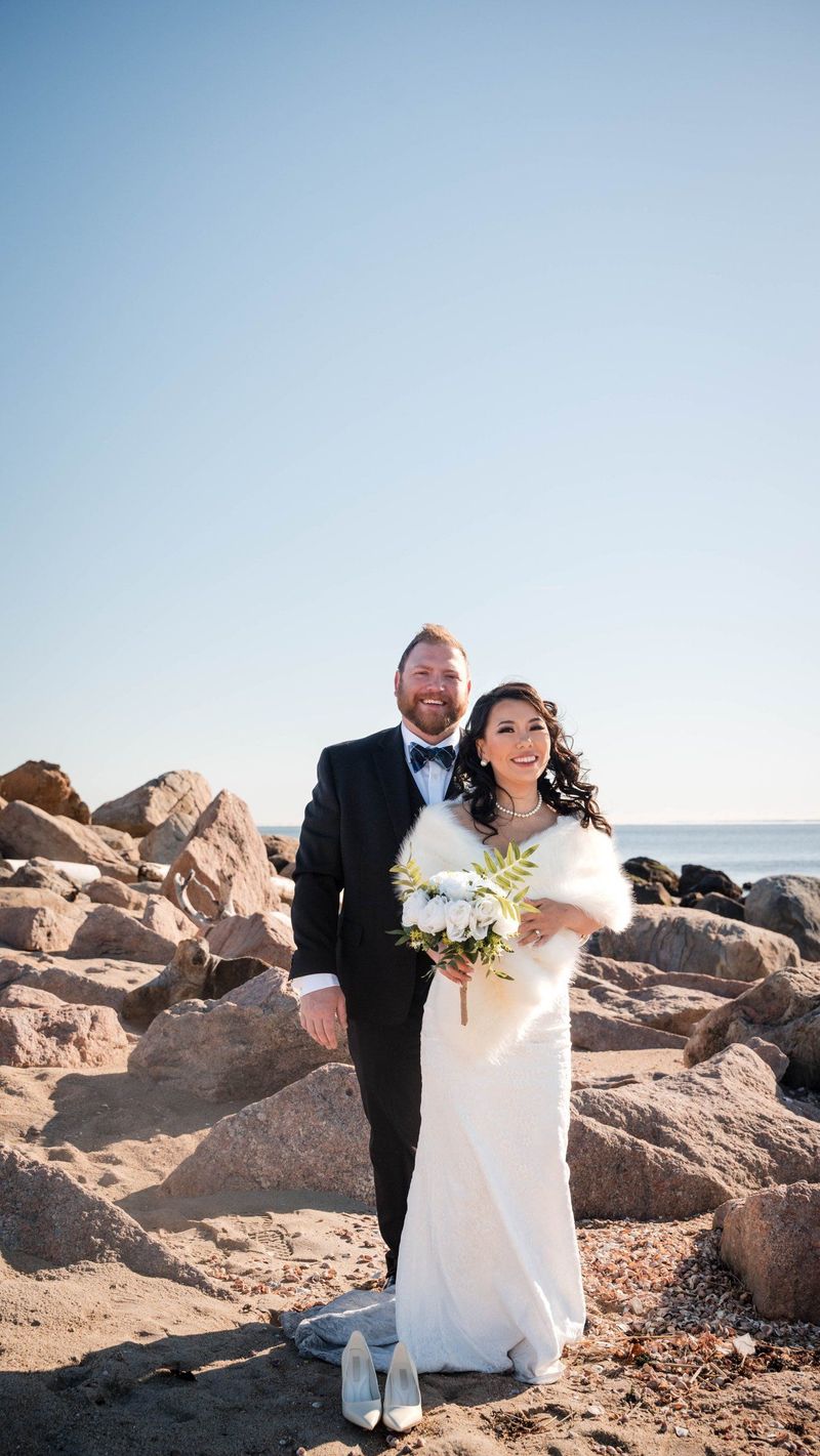 Amanda and Charles stand together among large shoreline rocks