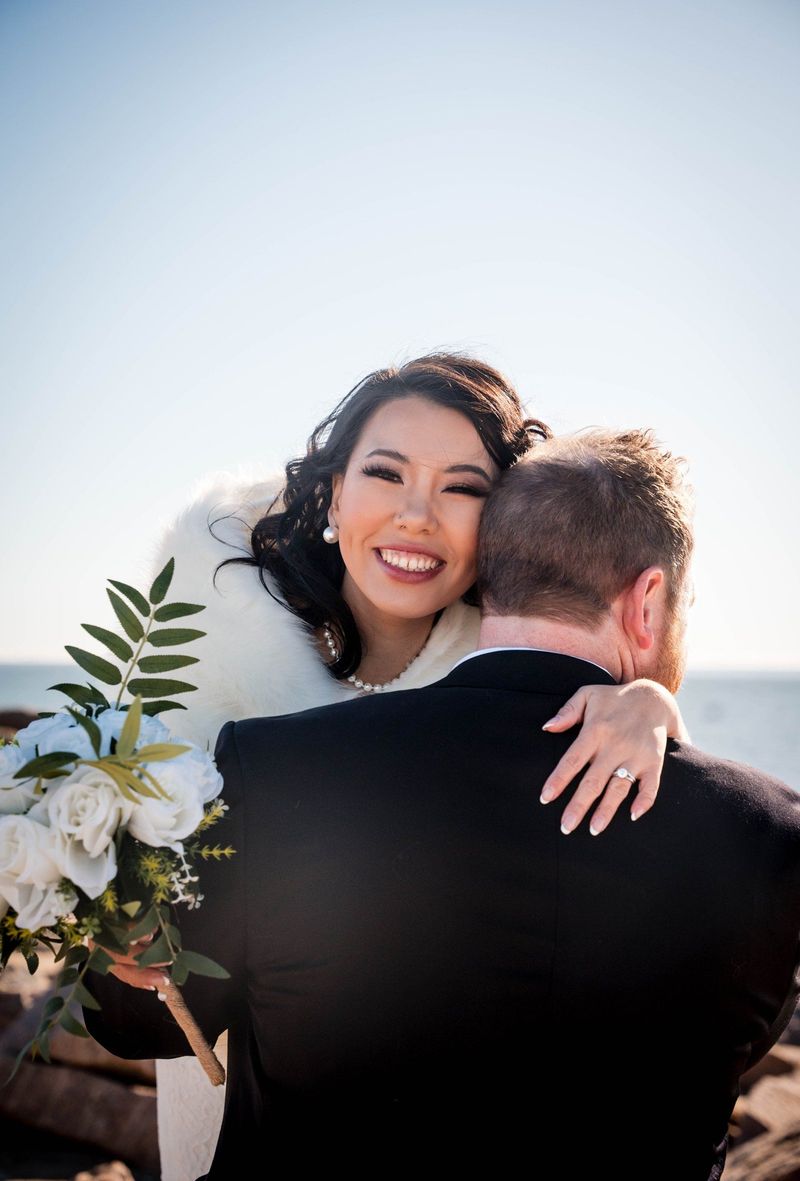 Amanda smiles over Charles’s shoulder during an embrace by the shoreline