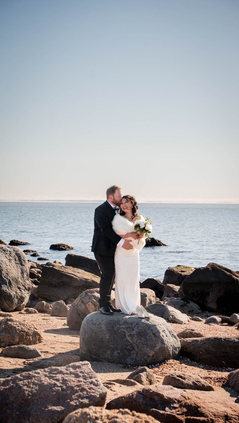 Amanda and Charles share a kiss on a large rock beside the water