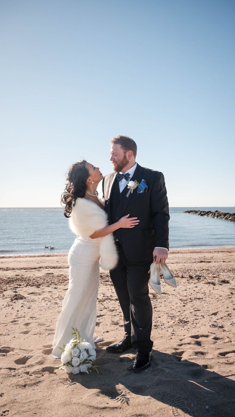 The couple face one another on the beach with the bouquet resting on the sand