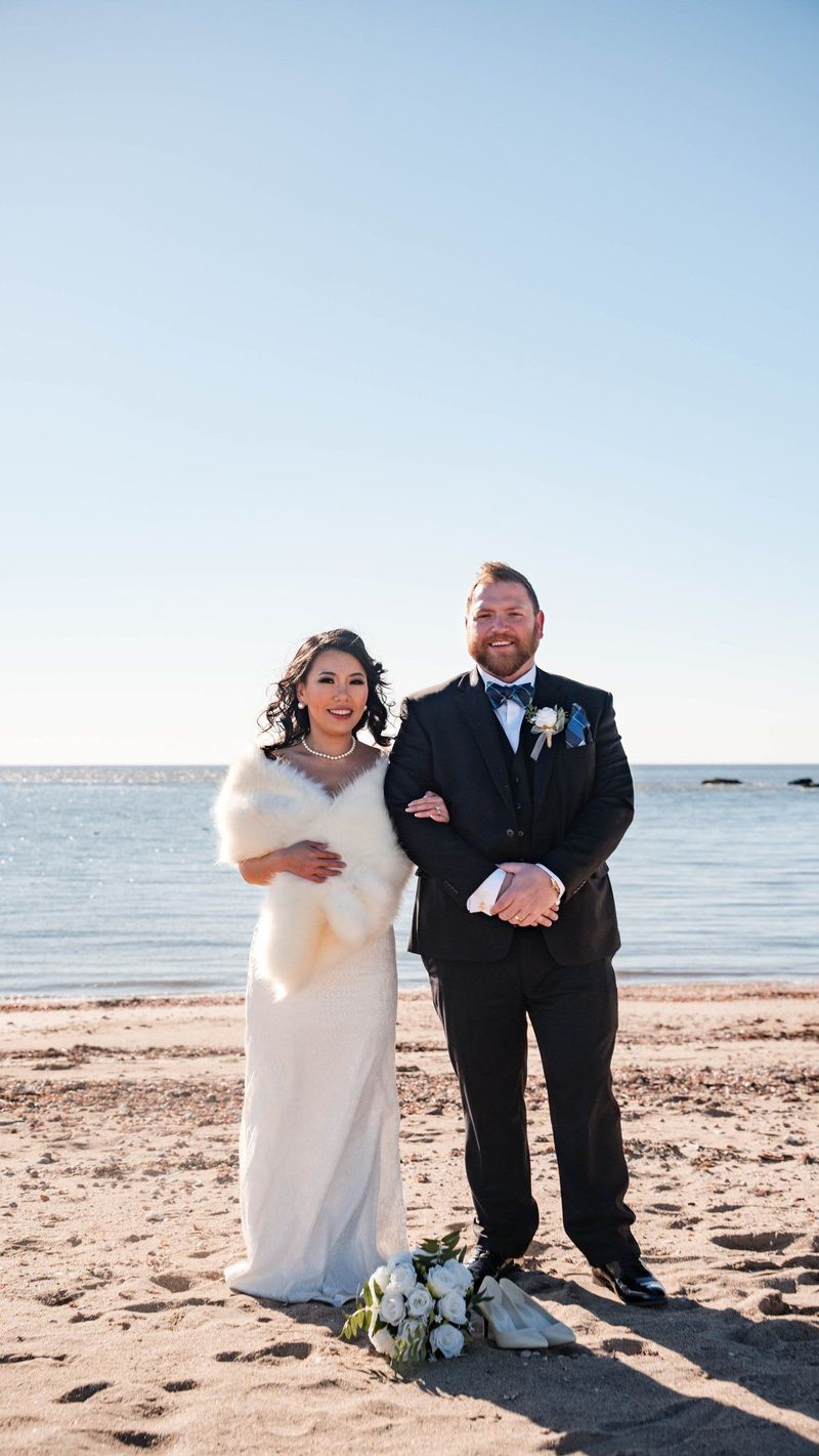 Amanda and Charles stand arm in arm on the sand
