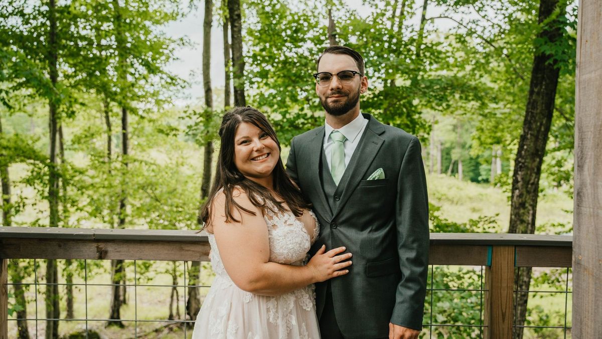 Ashley and Anthony together on the deck with green trees behind them