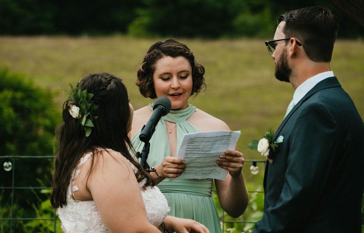 A reader holds a microphone and paper during the outdoor ceremony