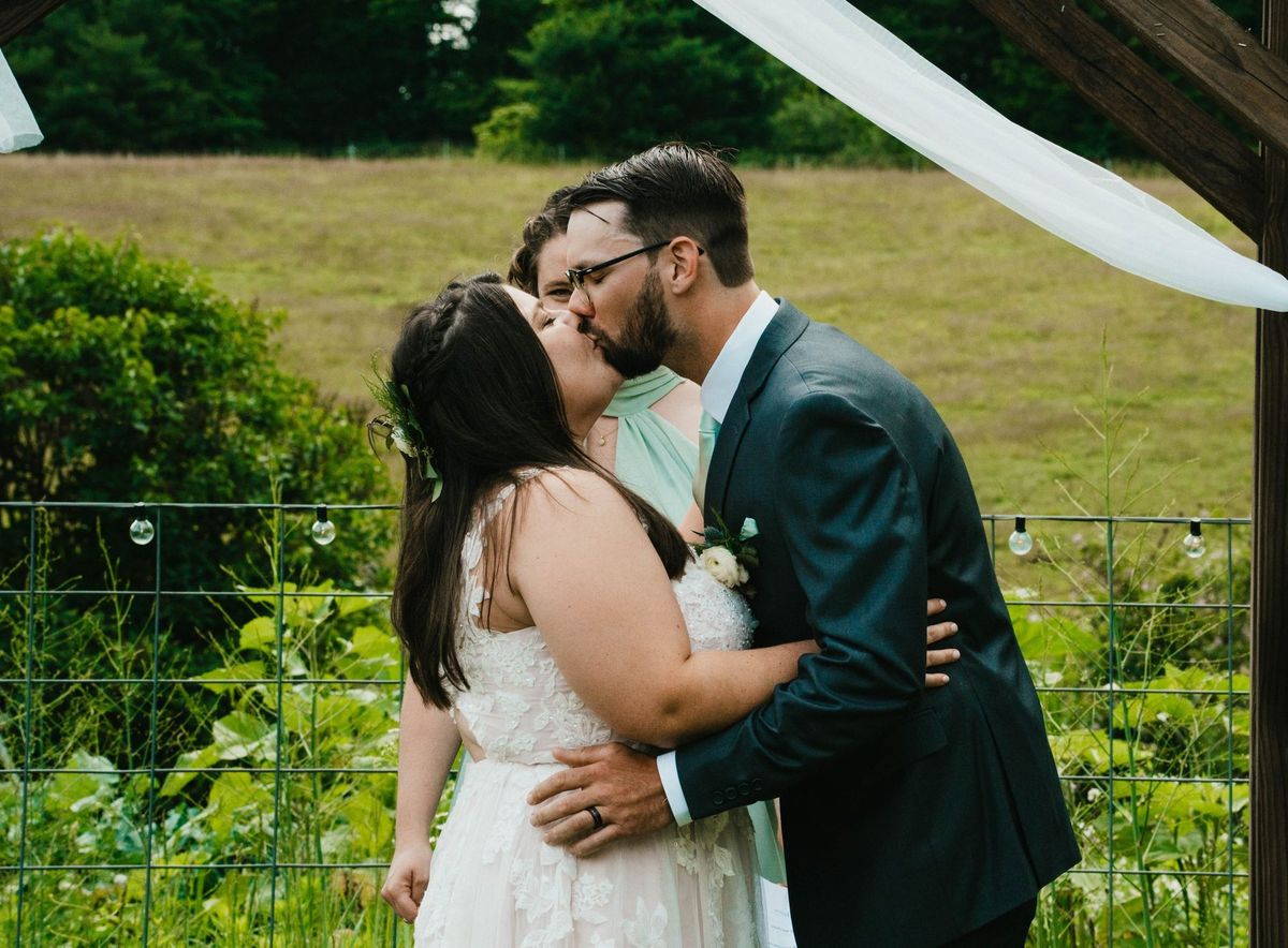 Ashley and Anthony kiss beneath the wooden ceremony arbor