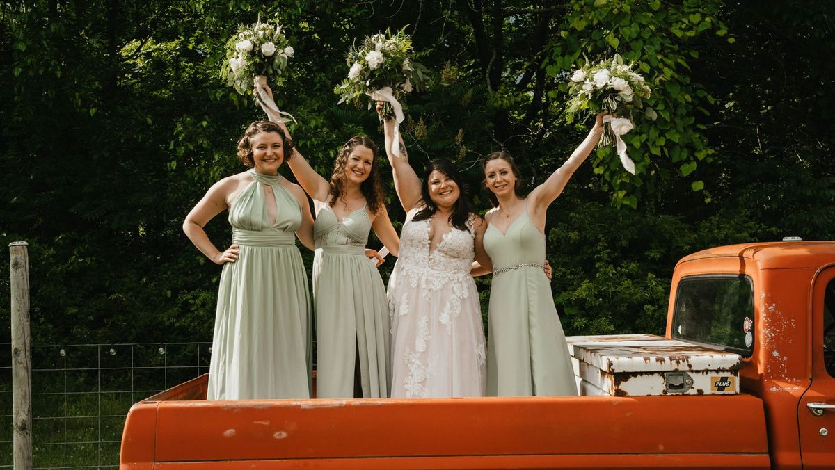 Ashley and her wedding party raise their bouquets from the orange pickup truck