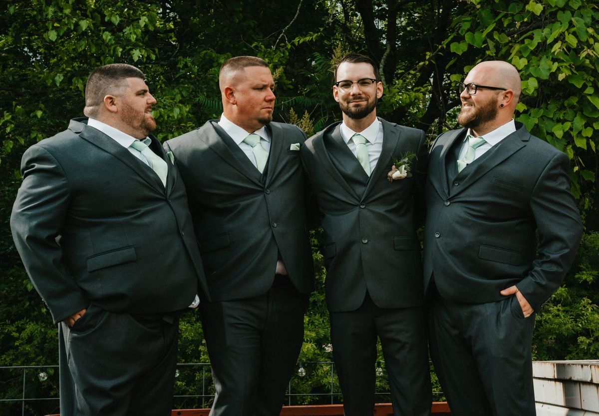 Anthony and the groomsmen smile together beside the orange pickup truck