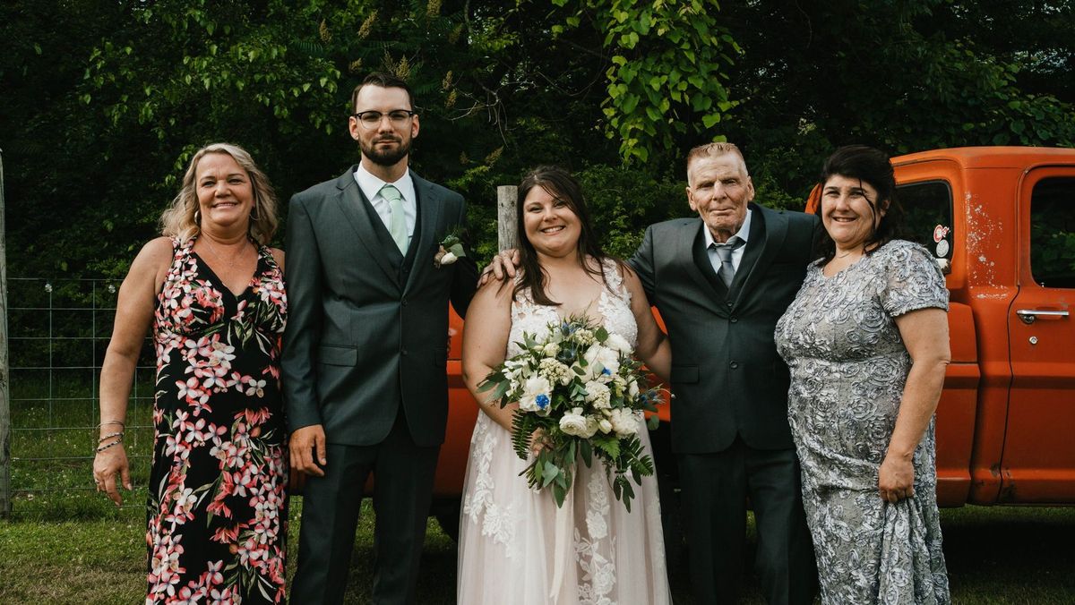 Ashley and Anthony pose with a small family group beside the orange truck