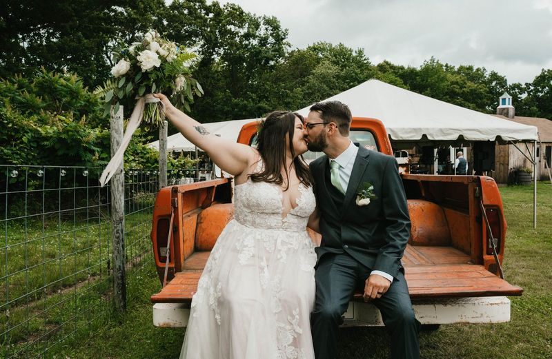Ashley and Anthony kiss on the tailgate as Ashley raises her bouquet